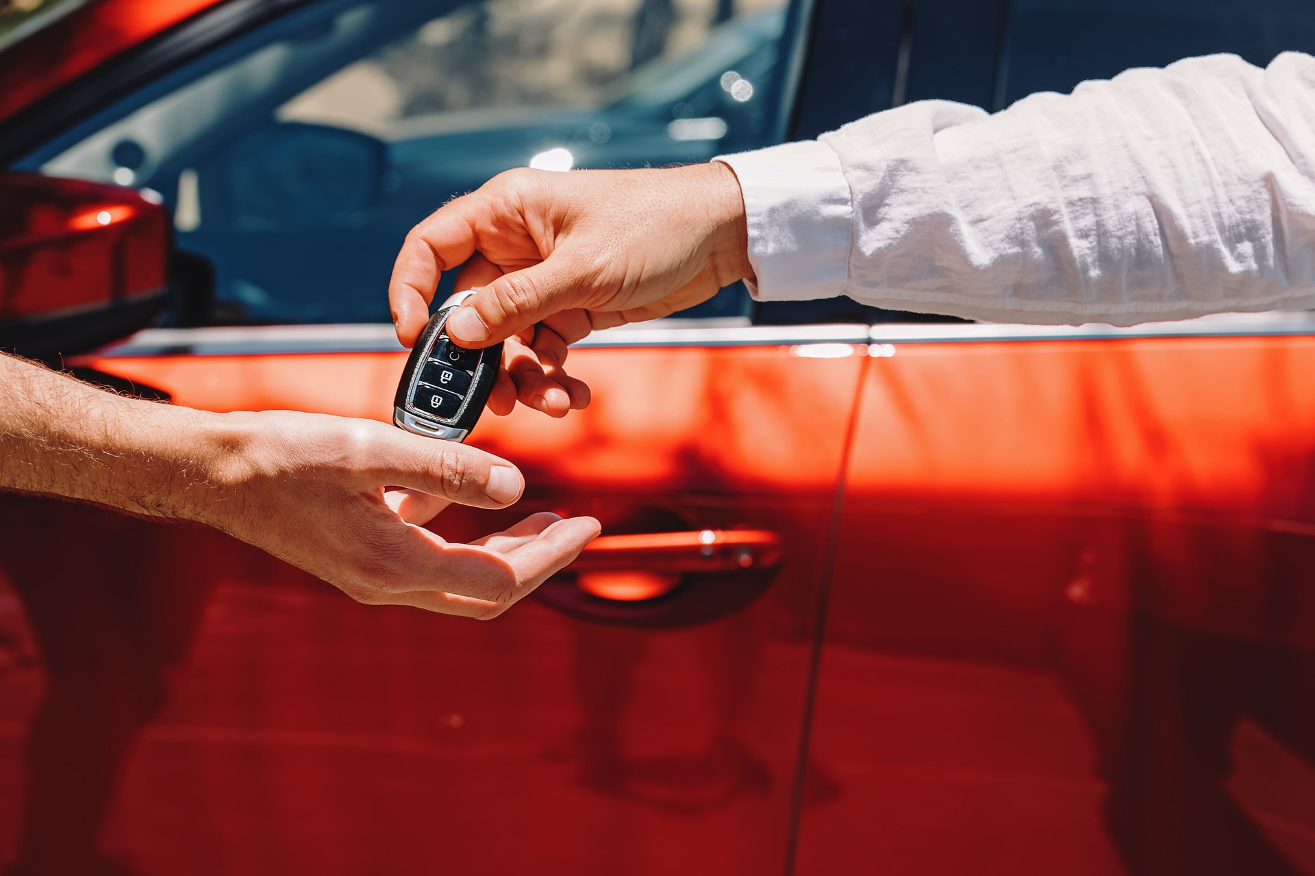Händler gibt Autoschlüssel an den neuen Besitzer. Nahaufnahme Von Händen Auf Dem Hintergrund Des Roten Automobils