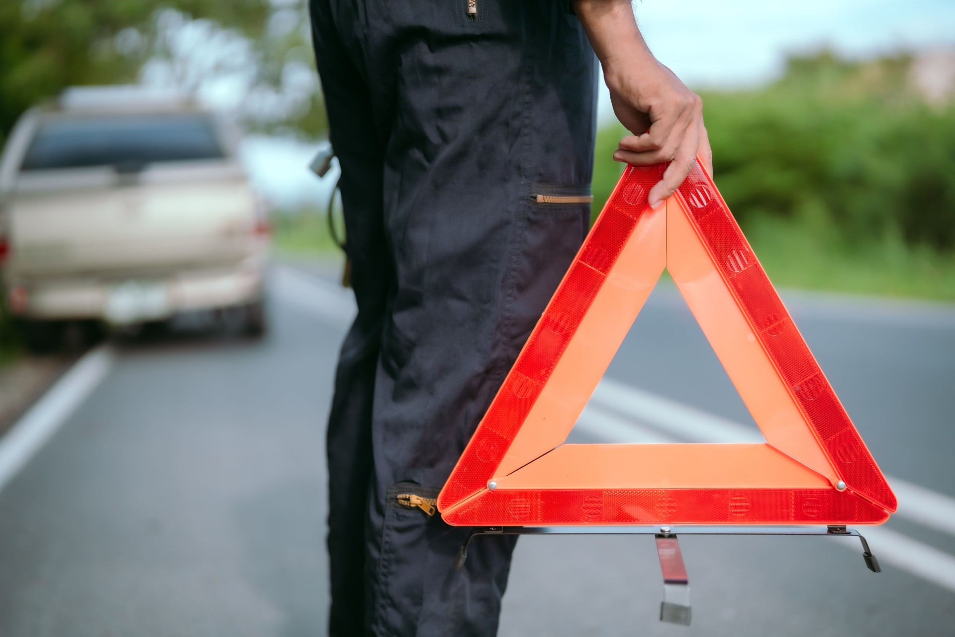 Roadside assistance at a vehicle breakdown with warning triangle in hand during daylight